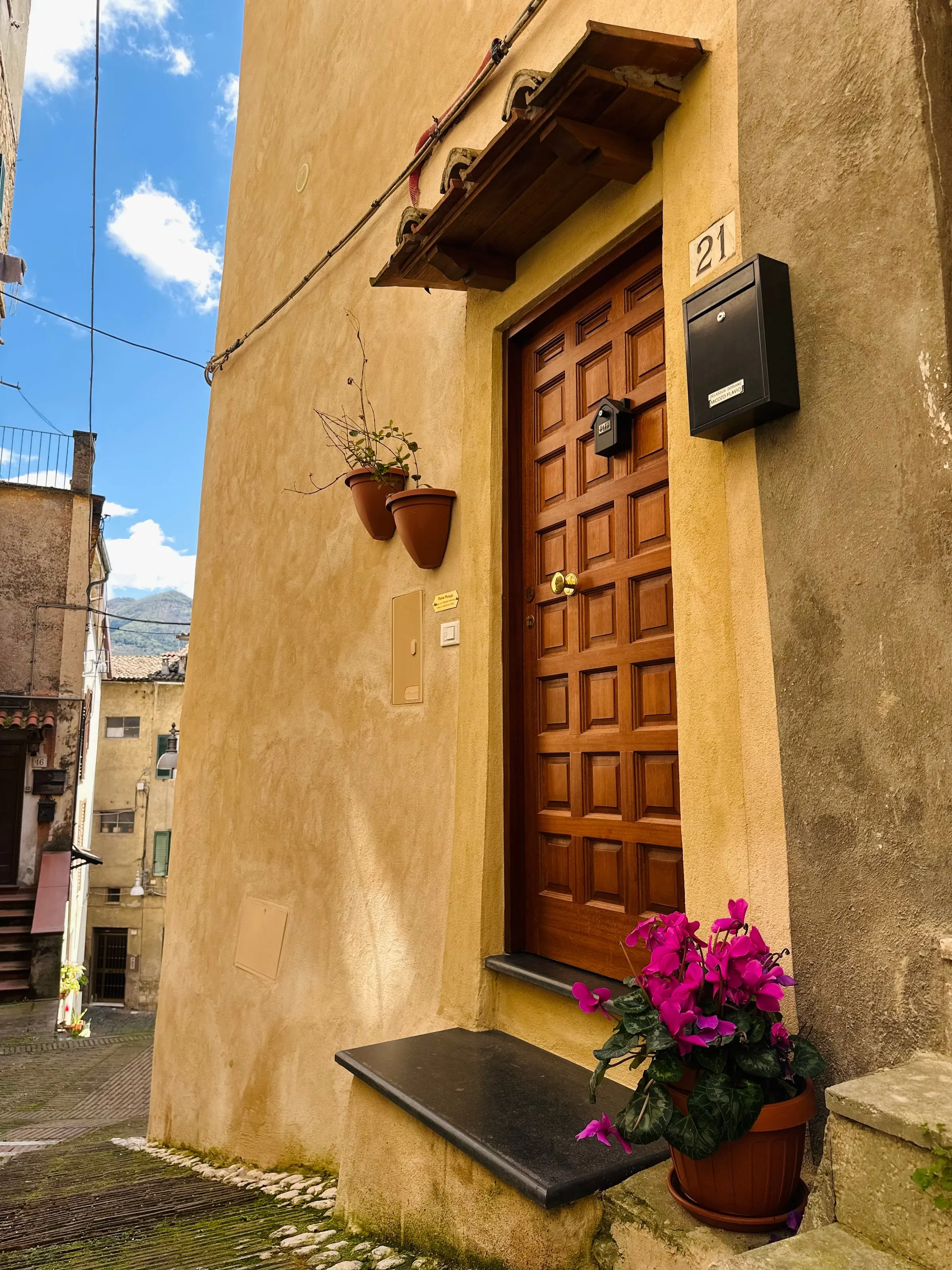 La facciata color ocra e la porta d’ingresso in legno, con vasi di fiori
